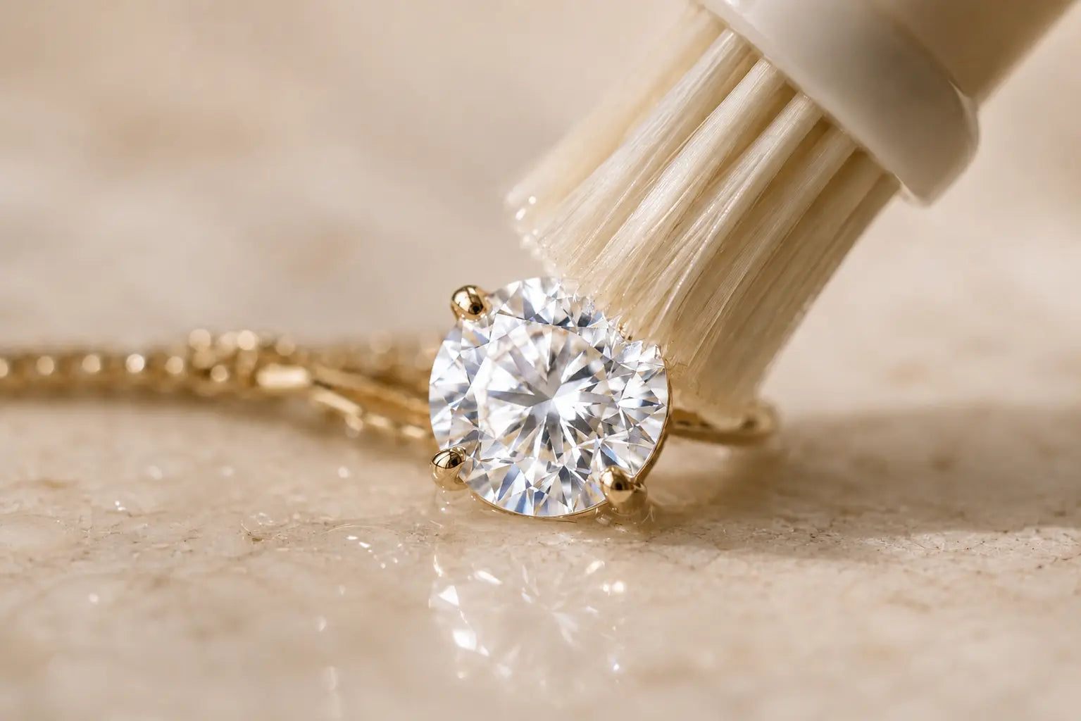 A soft brush cleaning a natural round brilliant diamond set in a solid 18K gold Aquae Jewels solitaire necklace