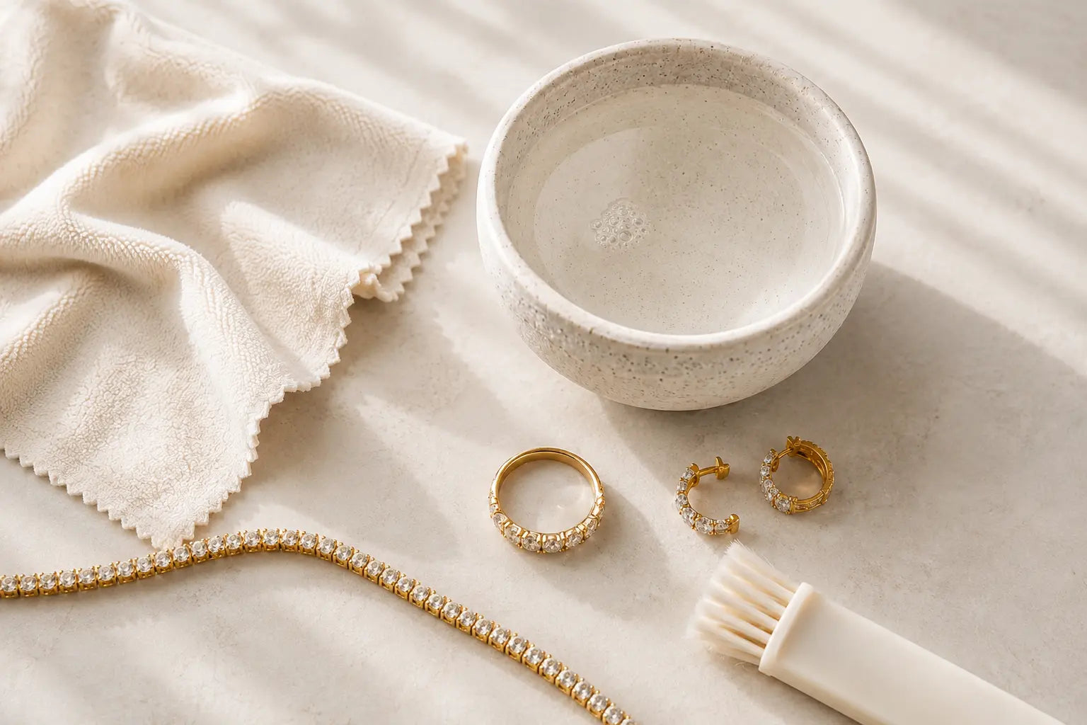 Aquae Jewels jewelry cleaning kit with a soft cloth, water bowl, brush, an 18K gold diamond ring, hoop earrings and tennis bracelet