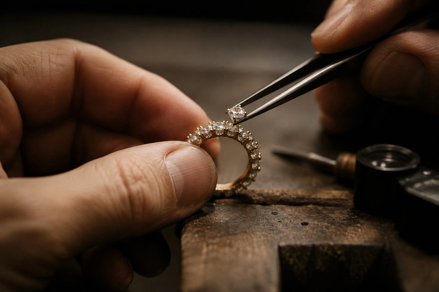 Master jeweler hand-setting a natural diamond into an 18K gold eternity ring at the workbench